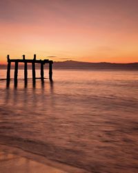 Silhouette wooden posts at beach against sky during sunset