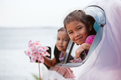 Portrait of cute girls leaning through car window at beach