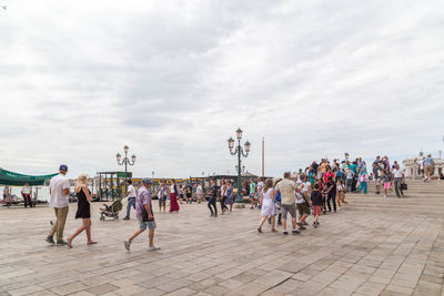 Group of people in city against cloudy sky