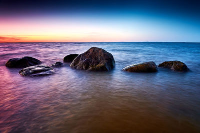 Rocks in sea against sky during sunset