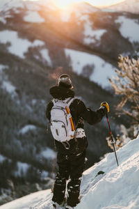 Rear view of man with skies standing on snow covered mountain during sunset