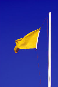 Low angle view of yellow flag on pole against clear blue sky