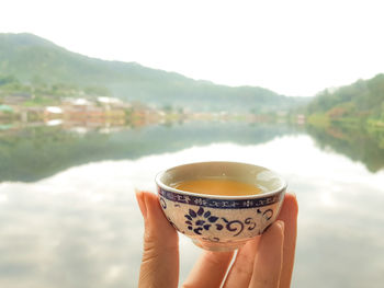 Close-up of hand holding tea cup against sky