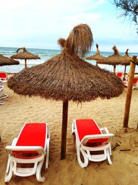 Lounge chairs and parasols on beach against sky