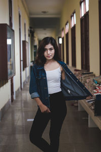 Portrait of confident young woman wearing denim jacket standing in corridor
