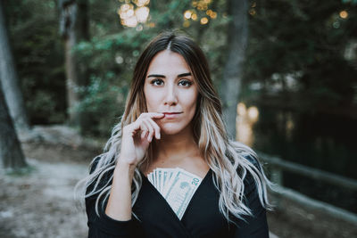 Portrait of beautiful young woman with paper currency standing in forest