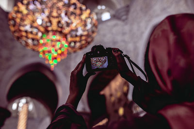 Close-up of woman photographing illuminated chandelier with digital camera