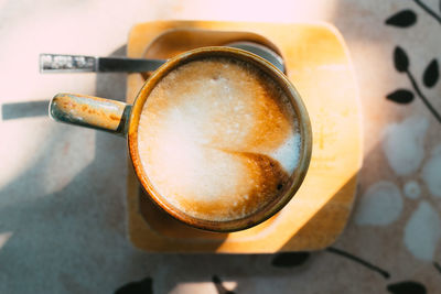 Cup of coffee latte with heart shape on old wooden background in the morning sunlight