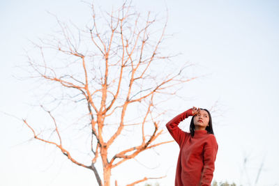 Woman standing by bare tree against sky