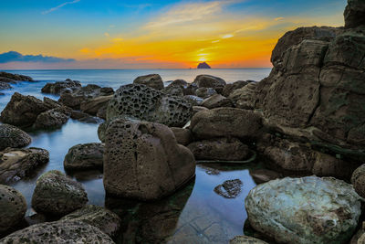 Rocks by sea against sky during sunset