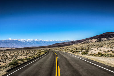 Empty road by mountains against clear blue sky