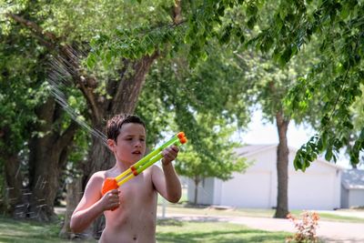 Full length of shirtless boy playing with plants against trees