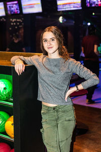 Portrait of smiling teenage girl standing by rack at bowling alley