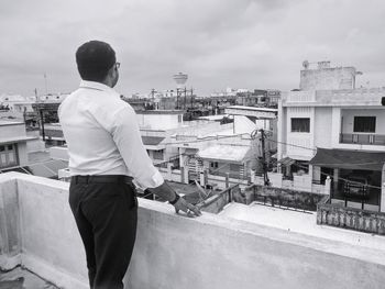 Rear view of man standing by buildings against sky