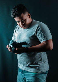 Young man with holding camera while standing against black background