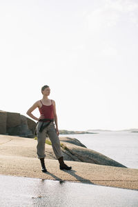 Full length of woman in sports clothing standing on rock at seaside