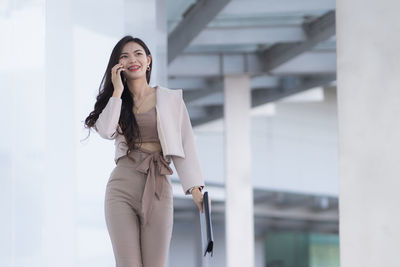 Smiling young woman talking on phone while walking outdoors