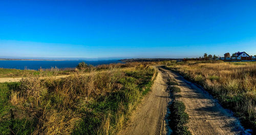 Surface level of dirt road leading towards sea against blue sky