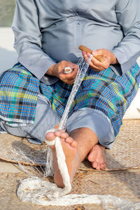 Old man is knitting traditional fishing net, hands and feet in frame