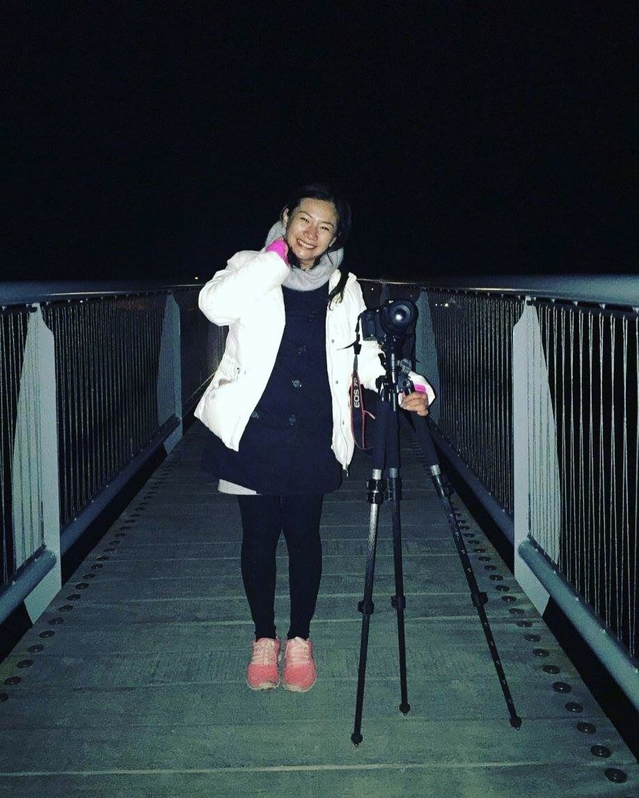 FULL LENGTH PORTRAIT OF YOUNG WOMAN STANDING AGAINST RAILING