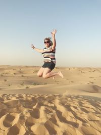 Woman jumping in desert against clear sky