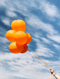 Low angle view of person holding balloons against sky