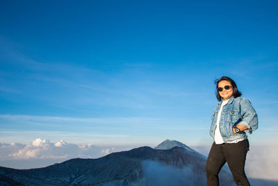 Portrait of smiling woman standing on mountain against blue sky