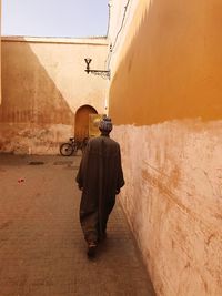 Rear view of man wearing traditional clothing while walking by wall
