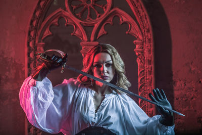 Portrait of woman in costume holding sword at abandoned building during night