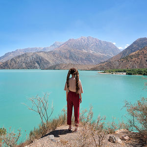 Rear view of man standing by lake against mountains