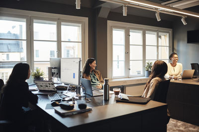 Happy female entrepreneurs communicating with each other while sitting at desk in office