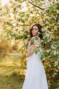 A cute happy young woman with a hairstyle in a white dress is walking enjoying nature in the summer