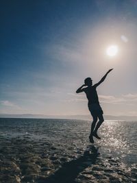 Silhouette of man jumping at beach against sky during sunset