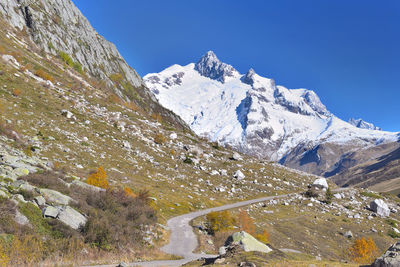 Road crossing mountain with snowy peak background under blue sky in euroean alps