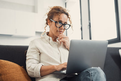 Young woman using laptop while sitting on sofa at home