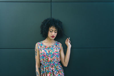 Fashionable young woman with curly hair against wall