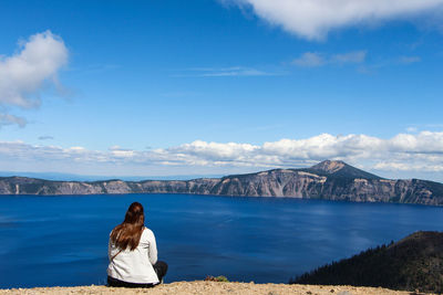 Rear view of woman looking at mountains against sky in crater lake