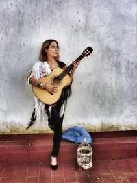 Young woman playing guitar against wall