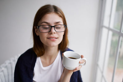 Close-up of woman holding coffee cup by window