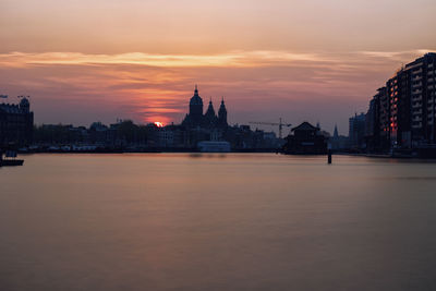 View of buildings by river against sky during sunset