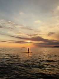 Silhouette woman paddleboarding on river against sky during sunset