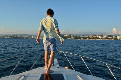 Rear view of young man on sailboat sailing in sea against sky