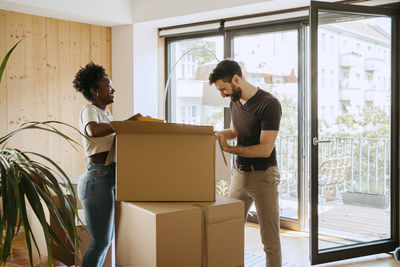 Happy multiracial couple unpacking boxes while standing at new home