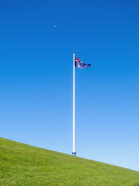 Low angle view of flag on field against clear blue sky