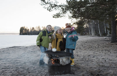 Mother and her kids eating marshmallows by a campfire at the beach