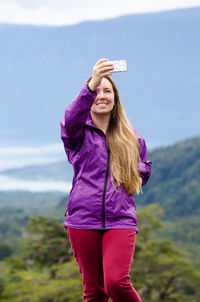 Woman taking selfie through mobile phone while standing against mountains