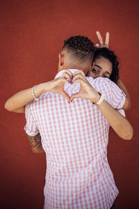 Couple gesturing while embracing while standing against red wall