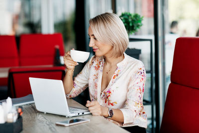An elegant business woman drinks coffee, works in a cafe, uses a laptop, enjoys a break. 