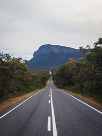 Empty road leading towards mountains against sky