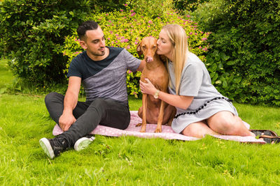 People relaxing on grassy field with dog